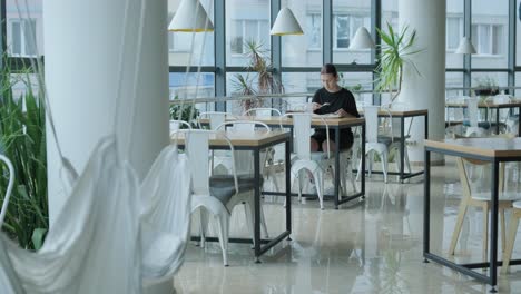 young woman eating a fresh salad at a wooden table in a modern restaurant with large windows, natural light, and urban views. relaxed dining scene