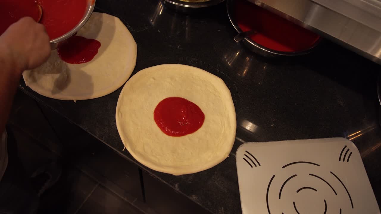 sobre la vista del hombro de un chef poniendo salsa de tomate en varias pizzas. cocinero haciendo múltiples pizzas en el restaurante