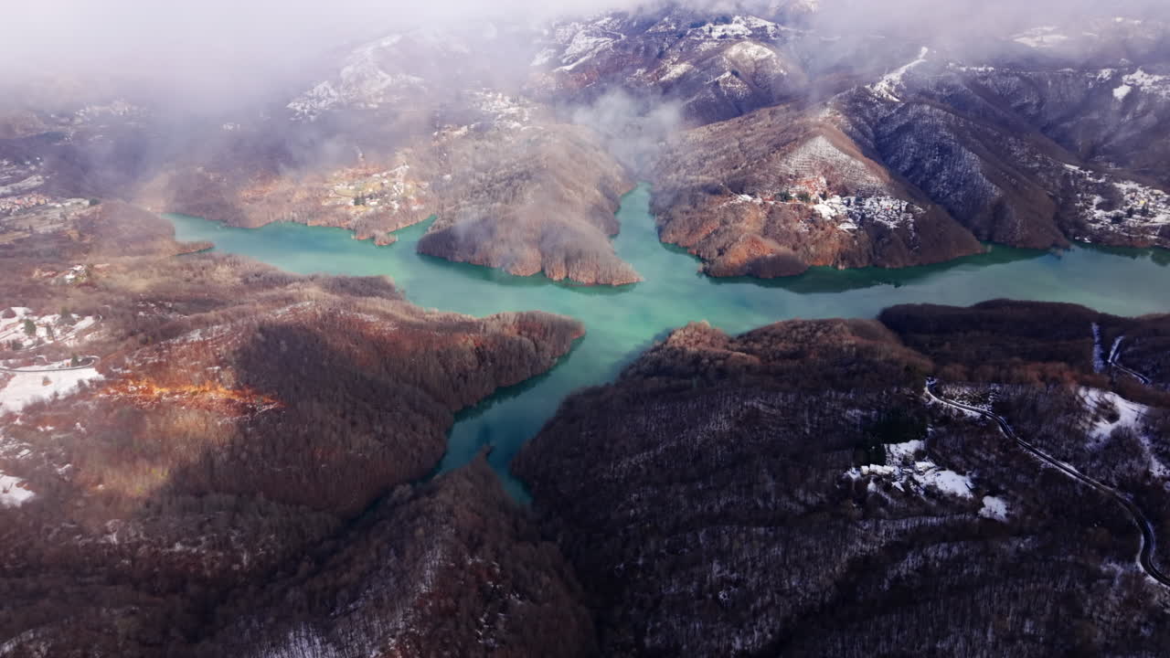 Montagne innevate e fiume color verde acqua sotto un cielo nuvoloso con un'atmosfera serena.