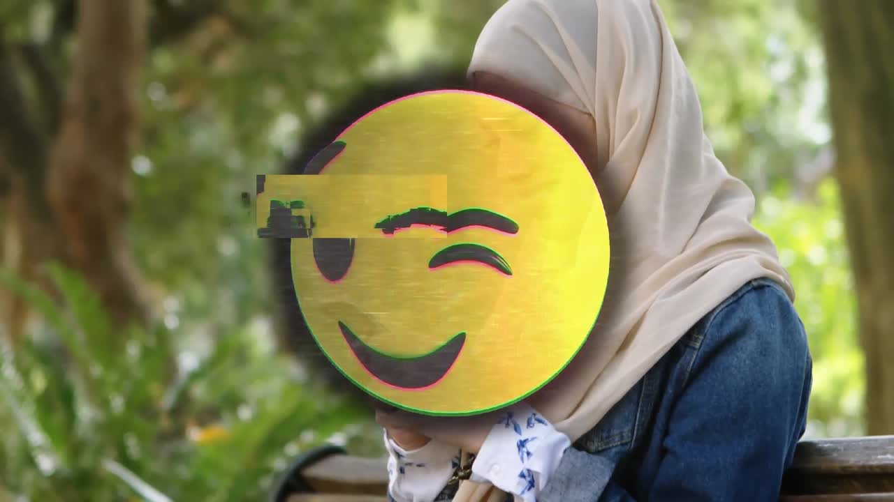 Animation of happy emoji over woman in hijab using smartphone