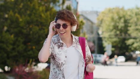 happy relaxed tourist man in wireless headphones dancing listening music walking in city street