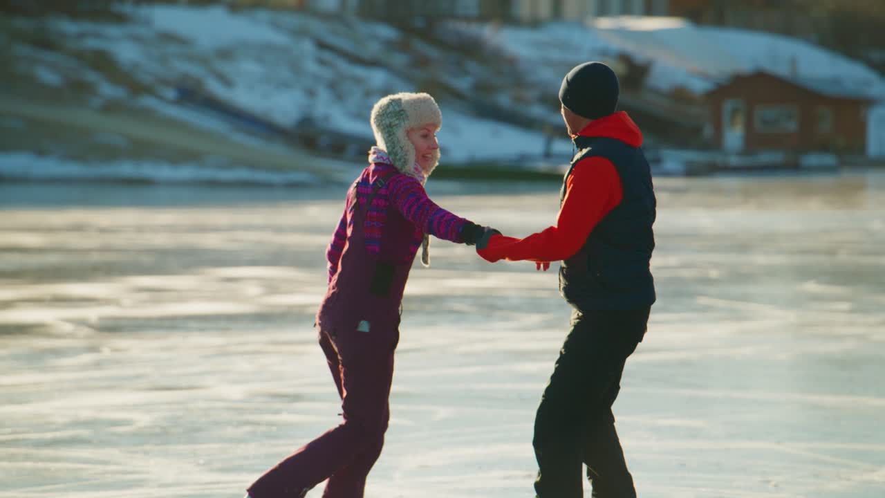Ett par som njuter av en vinterdag på isen, där de leker och dansar skridskodans tillsammans, håller varandras händer och tar sig fram på den frusna ytan, omgivna av vinternaturens lugna skönhet