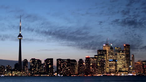 the lights of the toronto skyline glow brighter under a colorful darkening sky