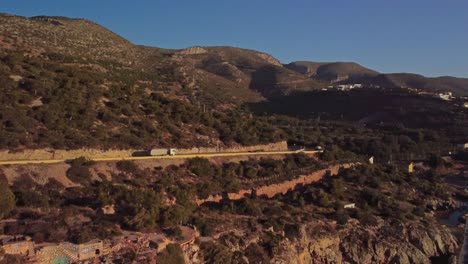 Scenic-coastal-road-with-cars-and-trucks-winding-through-rugged-hills-at-sunrise-in-Barcelona