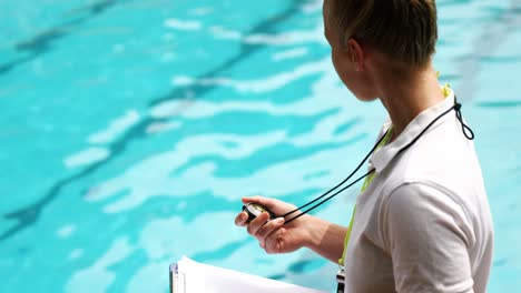 Swimming-coach-holding-clipboard-and-looking-at-stopwatch
