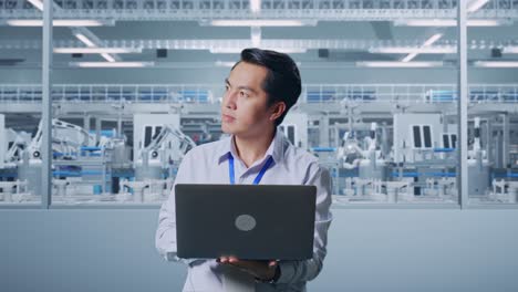 asian male professional worker standing with his laptop at factory digitalization, he observes by looking around before he come to concentrating with his laptop
