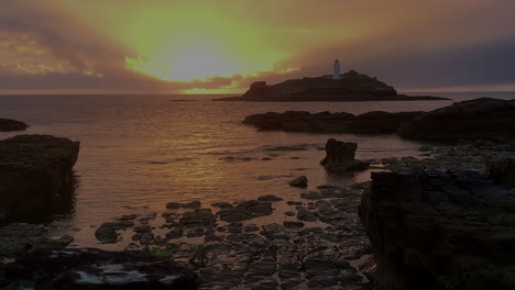 golden sunset light rays shimmering on sea waters at godrevy lighthouse, cornwall, wide shot.