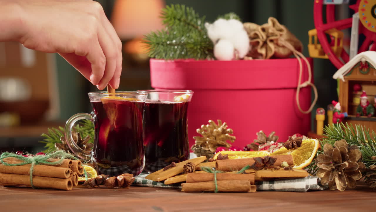 Hand rührt Glühwein mit Zimtstange inmitten von Weihnachtsdekorationen um
