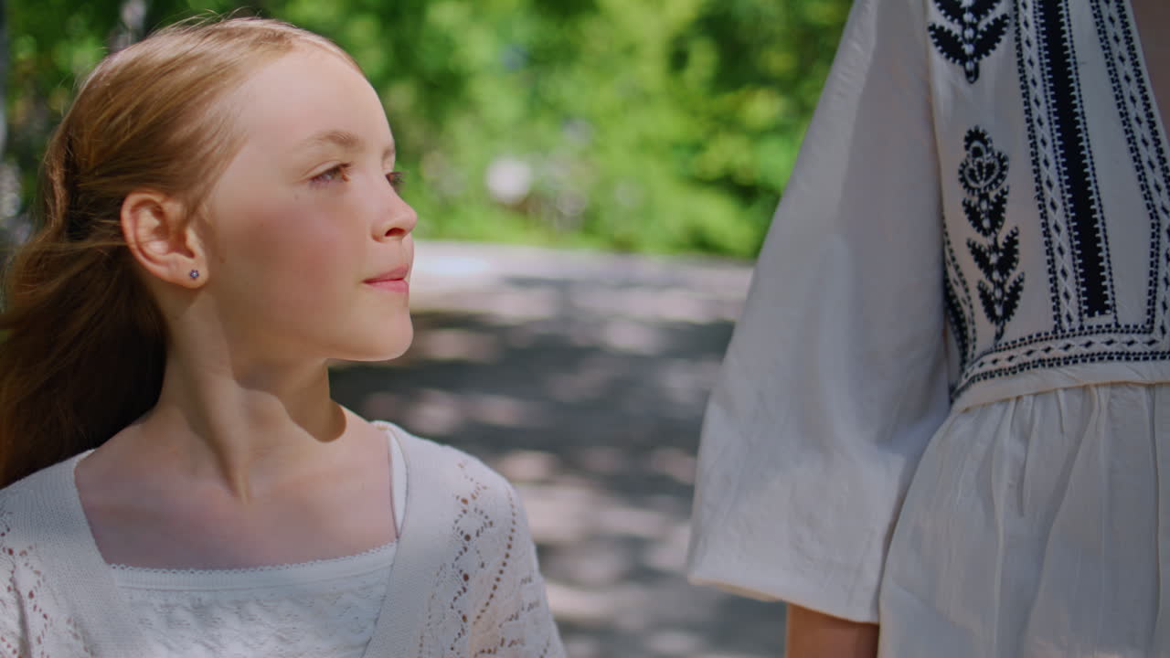 Cute daughter strolling park holding unknown mother hand at sunny day closeup