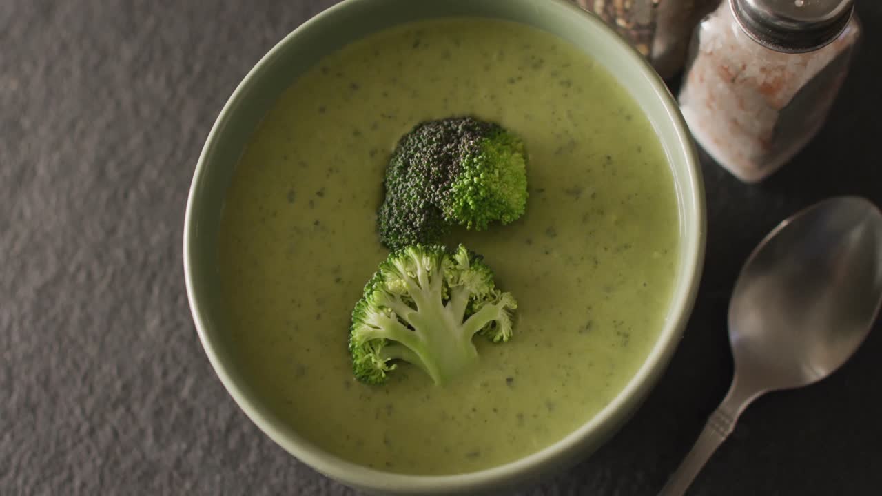 Video of cream broccoli soup in bowl on grey table with spoon and spices