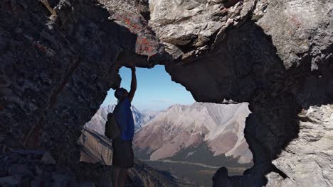 hiker touching rock admiring view trough hole arch on mountain kananaskis alberta canada