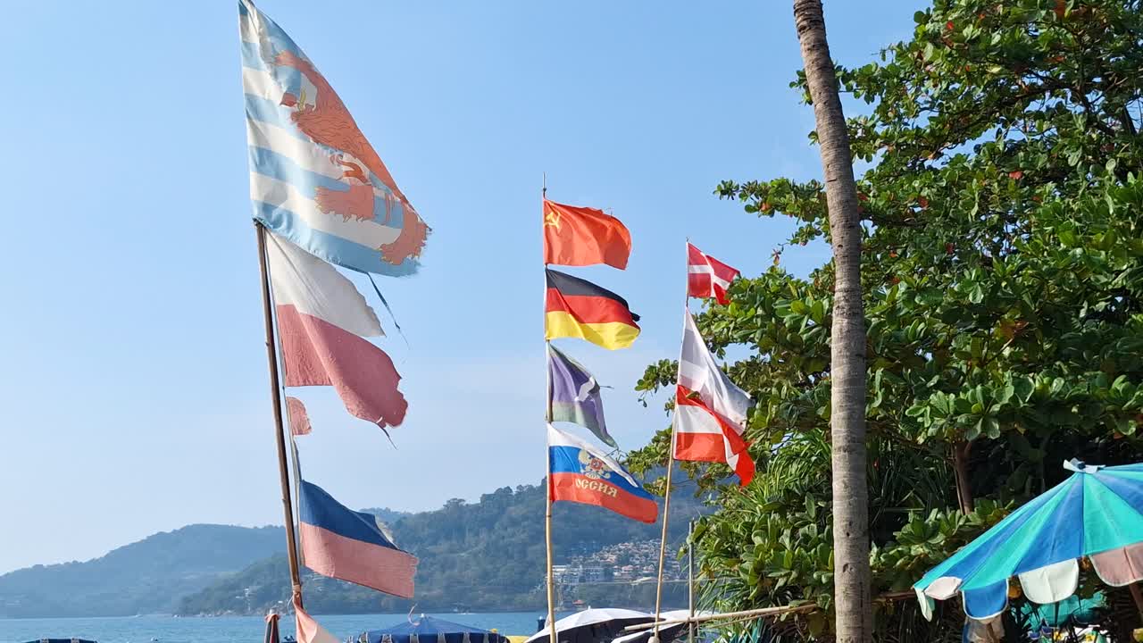 National flags waving at Patong Beach, Phuket, with a clear view of the coastline
