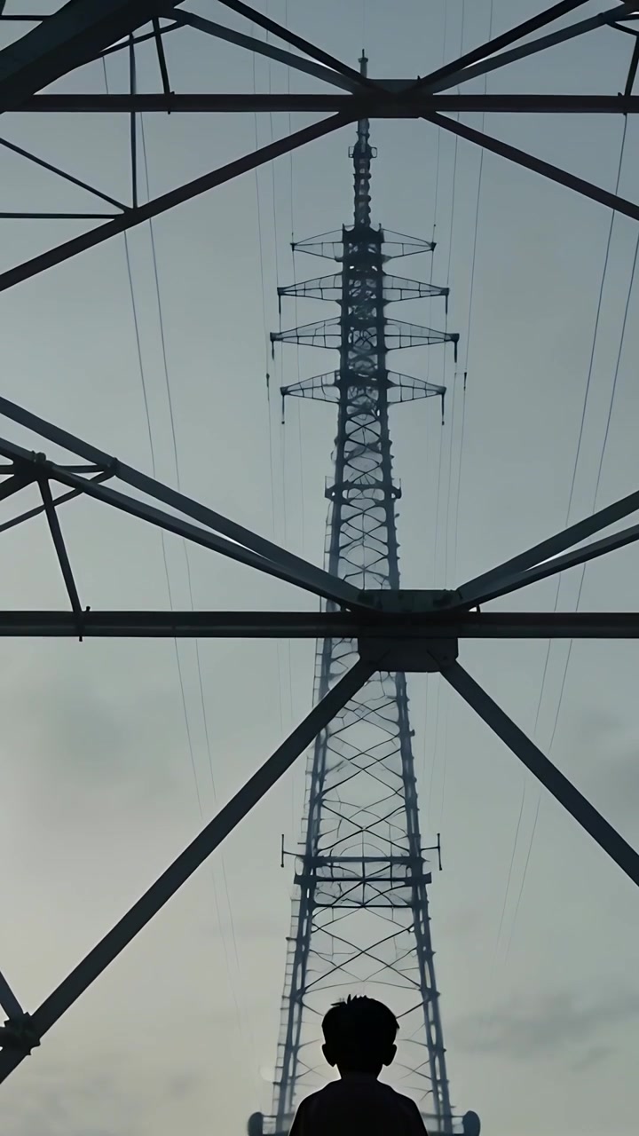 Vertical video: Tilting camera showing boy standing, looking up in tee under pylon to show height