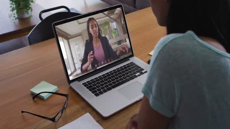 Mixed-race-businesswoman-sitting-at-desk-using-laptop-having-video-call-with-female-colleague