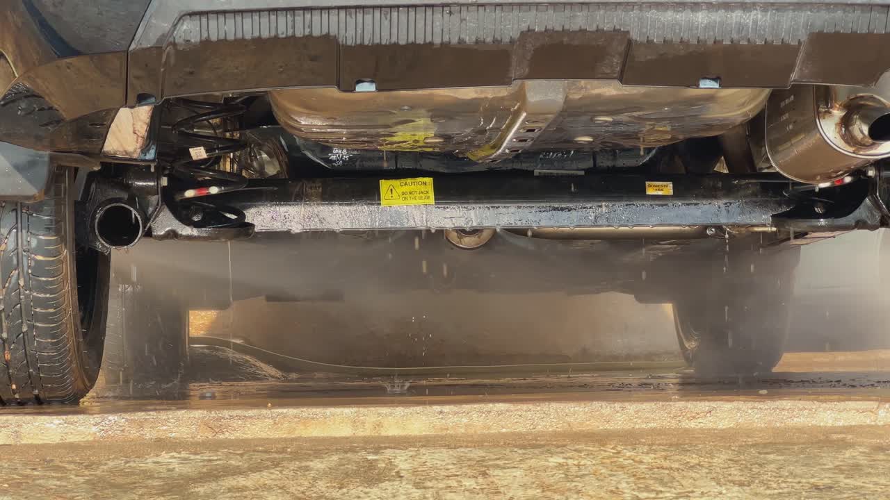 Mid shot of a high-pressure wash hose that is being directed toward the underbelly of the car where dirt hides and rust begins, ensuring even the hidden parts get a deep wash