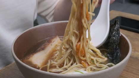 woman stiring up a ramen noodle soup with chopsticks