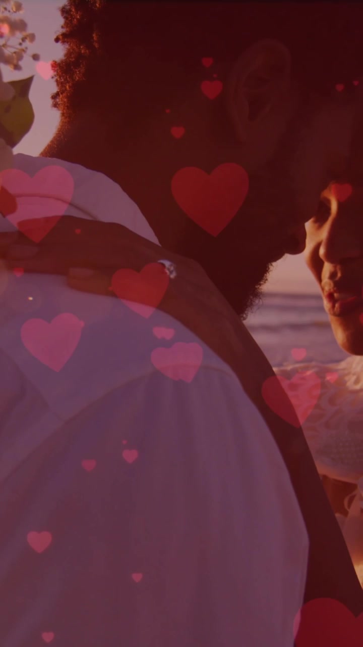Red hearts floating against african american newly married couple embracing each other at the beach