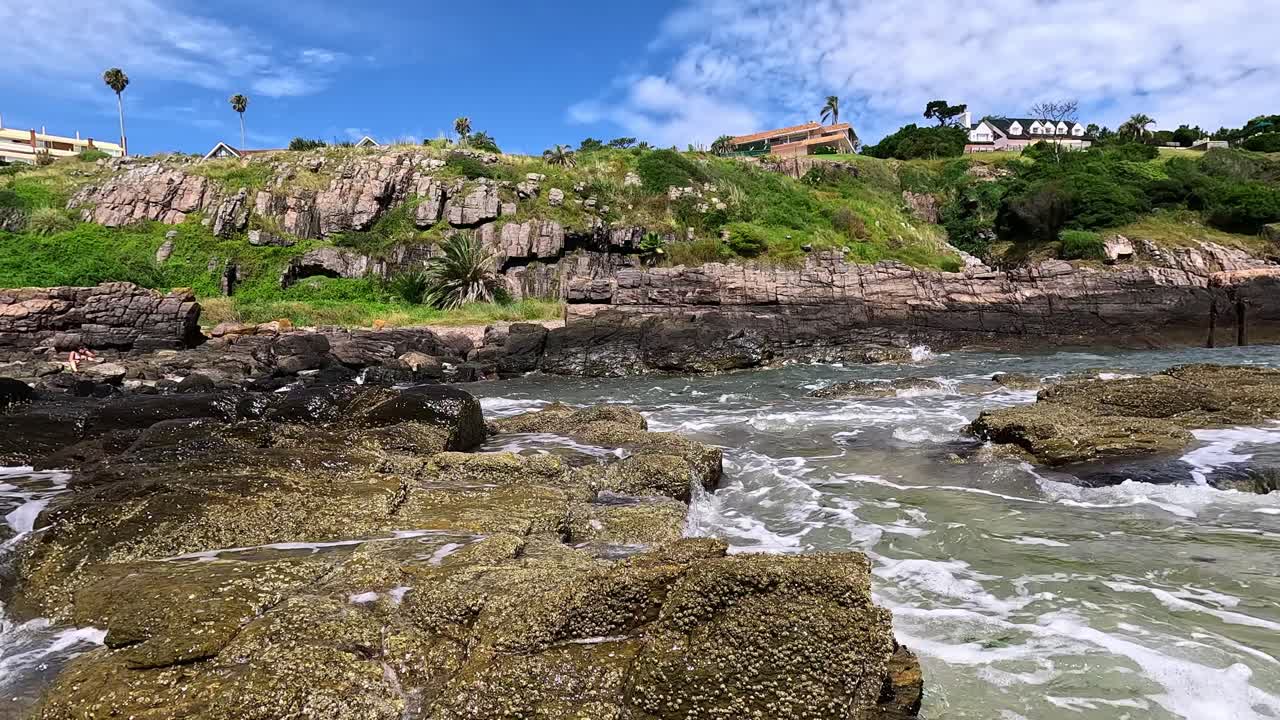 olas rompiendo contra los acantilados de punta ballena, mostrando mansiones en la cima de la colina, en uruguay