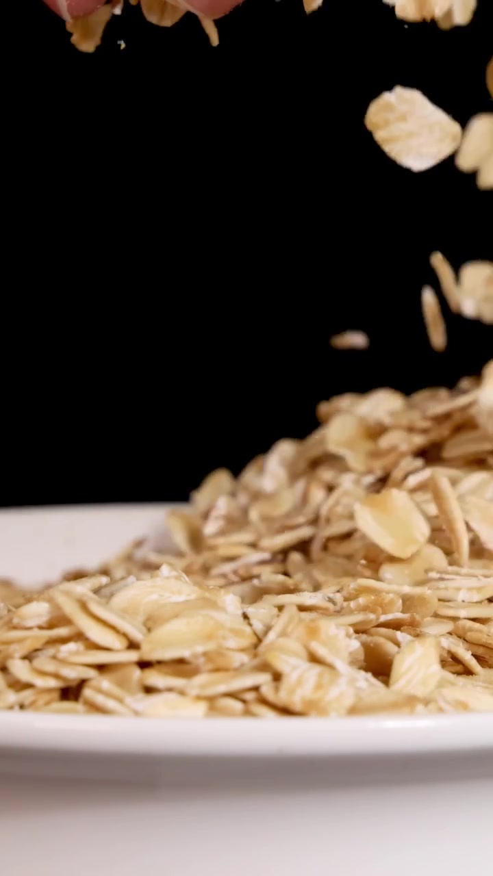 Una mano setaccia l'avena su un piatto, su uno sfondo nero, evidenziandone la consistenza e il movimento.
