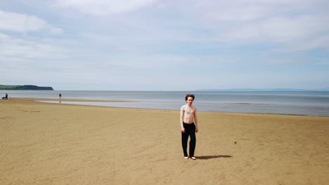 young man with no shirt and shoes walking on a sandy beach, aerial