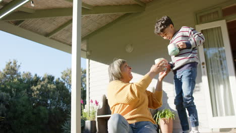 Feliz-Abuela-Birracial-Y-Nieto-Sosteniendo-Tazas-En-La-Terraza,-Cámara-Lenta