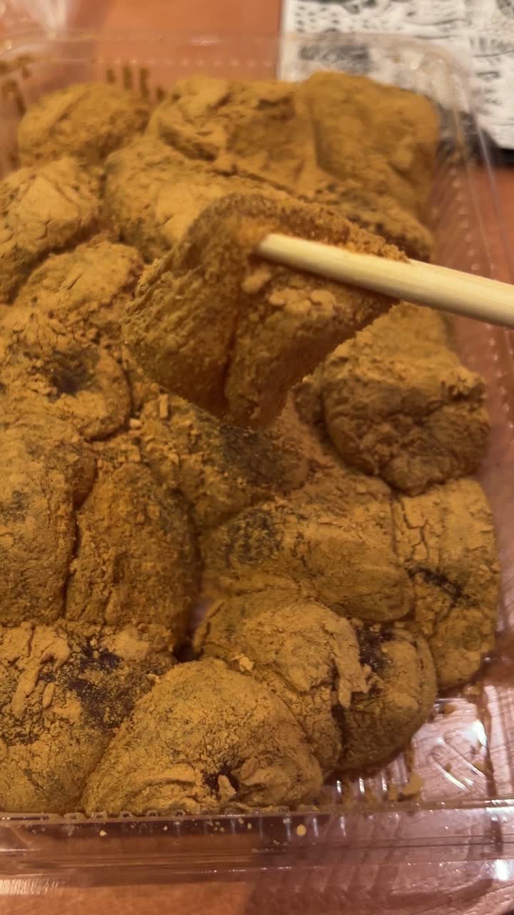 Bacchette che prendono Warabi Mochi con polvere di Kinako, dolcetti giapponesi Wagashi.
