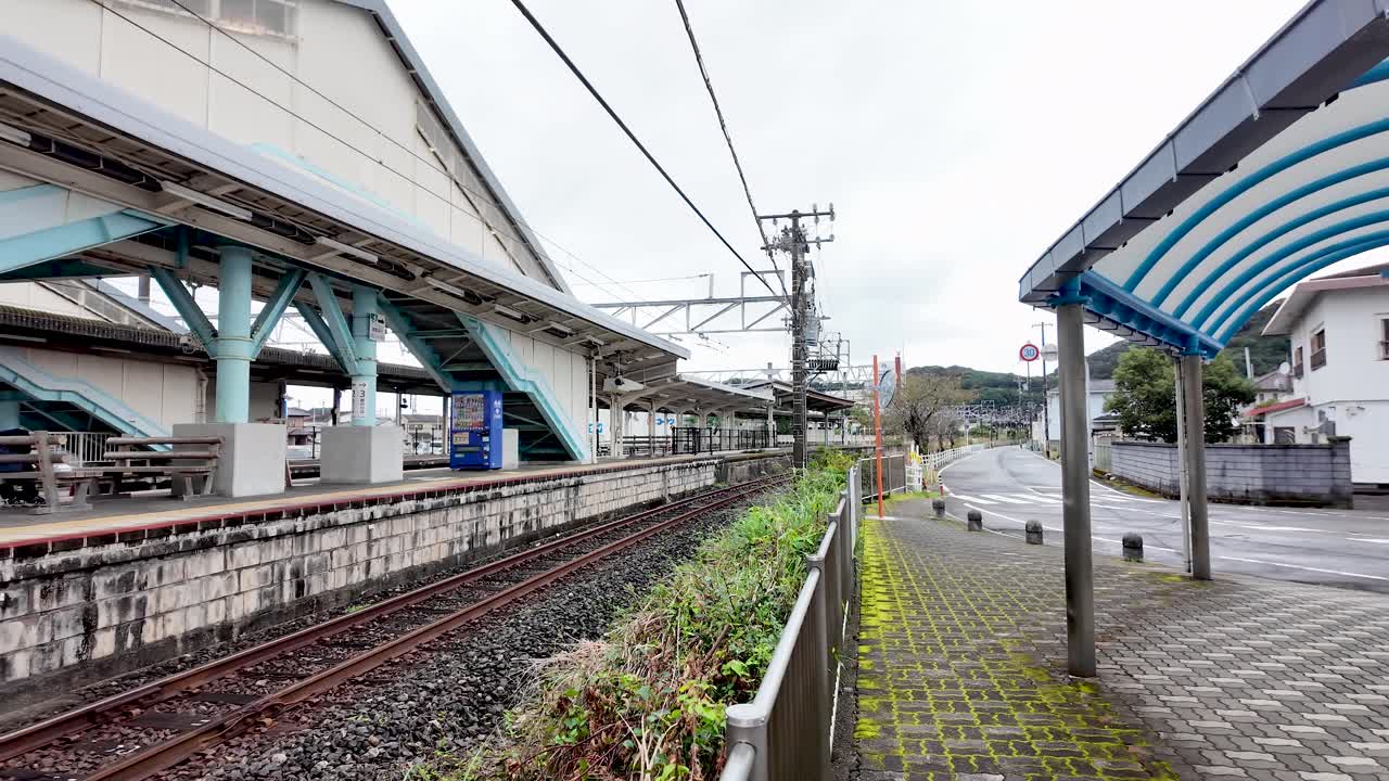 Empty platform at Kii Katsuura Station with railway tracks, overhead lines, and a street leading to a residential area in Japan