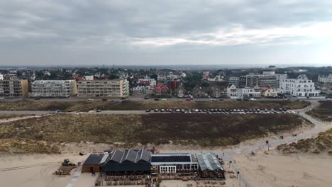 Beach Restaurant and parking cars in Noordwijk aan Zee Town, Netherlands. Apartment hotels and green yellow dunes. Aerial lateral wide shot.