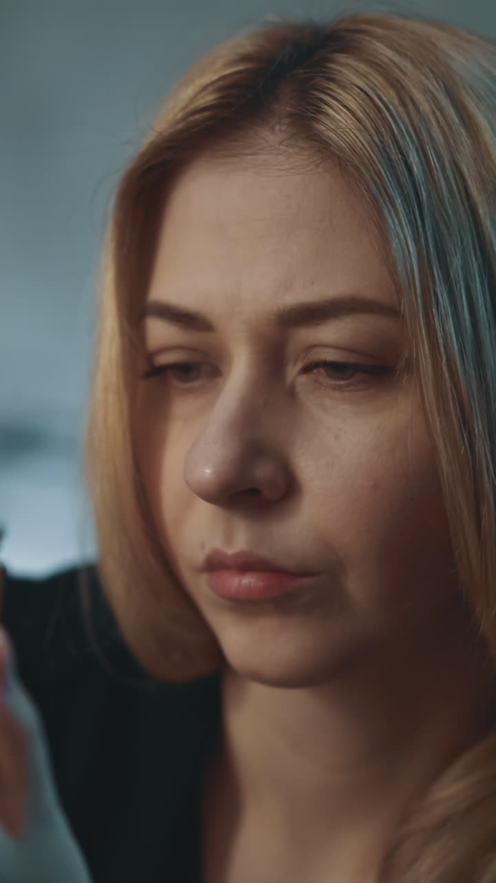 Pensive woman with long fair hair holds glass pill bottle with biologically active additives sitting on blurred background in darkened office close view slow motion