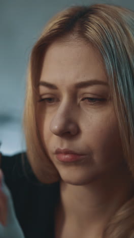 pensive woman with long fair hair holds glass pill bottle with biologically active additives sitting on blurred background in darkened office close view slow motion