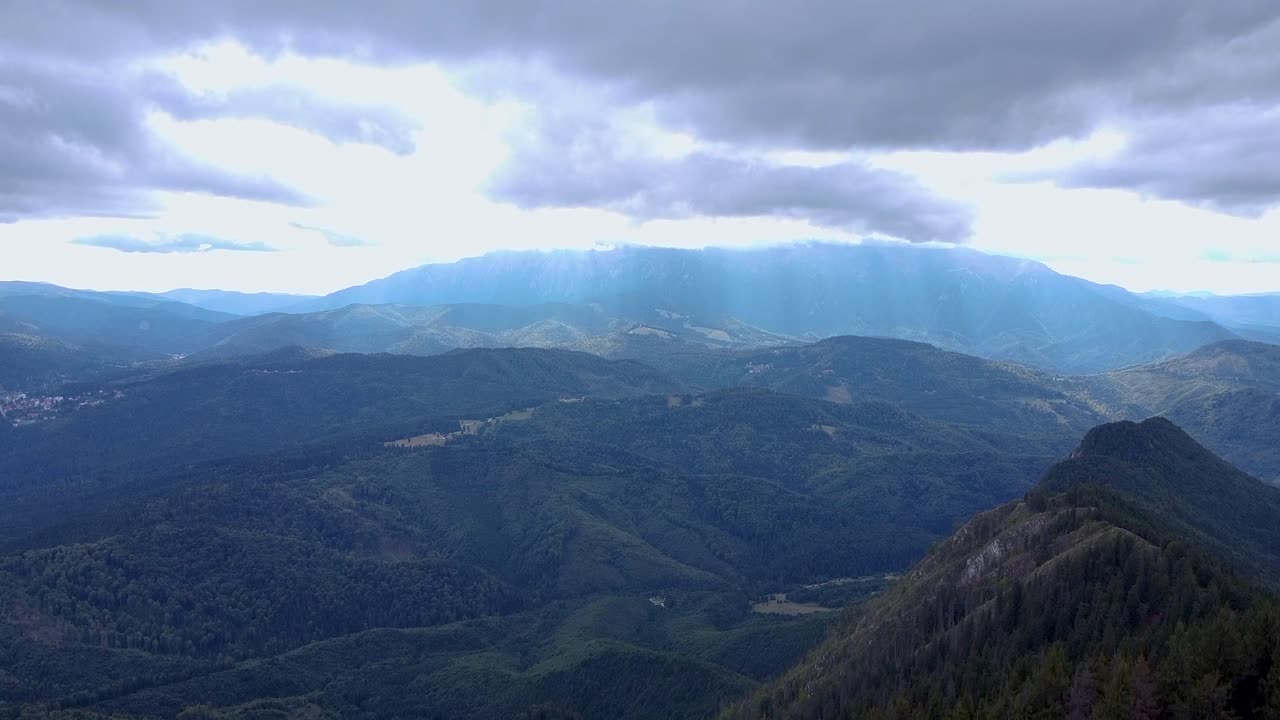 una impresionante vista aérea de un exuberante bosque verde de montaña con altos picos en el fondo rodeados de rayos solares y nubes blancas esponjosas, ubicado en poiana brasov, rumania