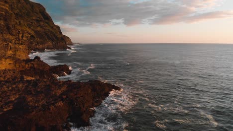 Hohe-Wellen-Spülen-Die-Klippen-Des-Piha-Strandes,-Die-Zur-Goldenen-Stunde-In-Warmen-Farben-Gestrichen-Sind