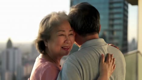 happy asian senior couple hugging on a city balcony
