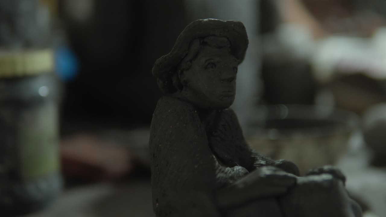 A clay sculpture of a seated figure in a dimly lit studio