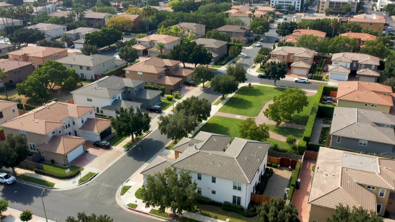 Dron a la deriva revelando más casas suburbanas y un parque rectangular en el centro, mostrando tejados.