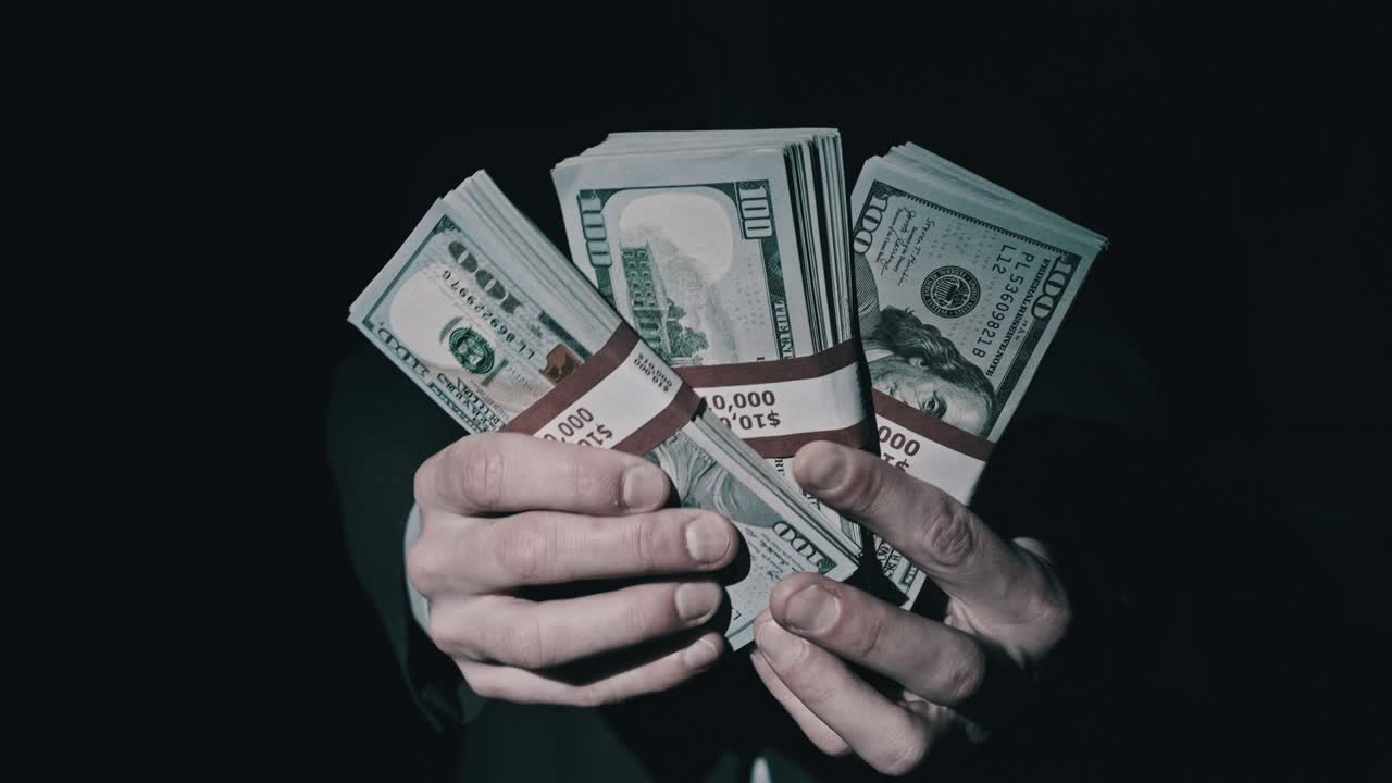 три стопки из 10000 американских долларов в мужских руках на черном фоне