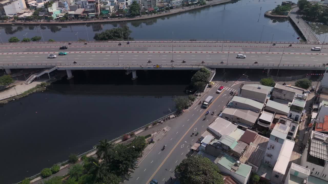Aerial view of busy freeway over river with urban sprawl on sunny clear day slow fly in to roadway