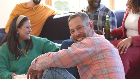 amigos felizes, homens e mulheres, a relaxar em casa, a beber cerveja e a comer pipocas.