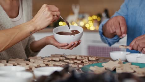 pareja multiétnica irreconocible decorando galletas dulces en casa durante la navidad.