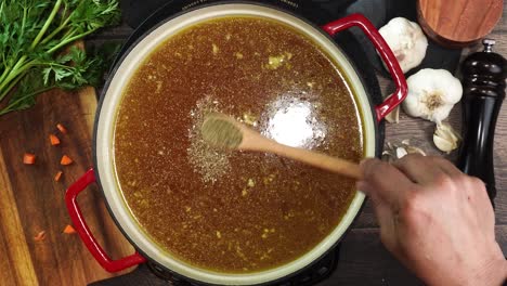 cooking italian wedding soup and adding spices like oregano or basil to the red stock pot. mixing in spices and herbs to soup. using a wooden spoon to stir the broth while simmering soup.