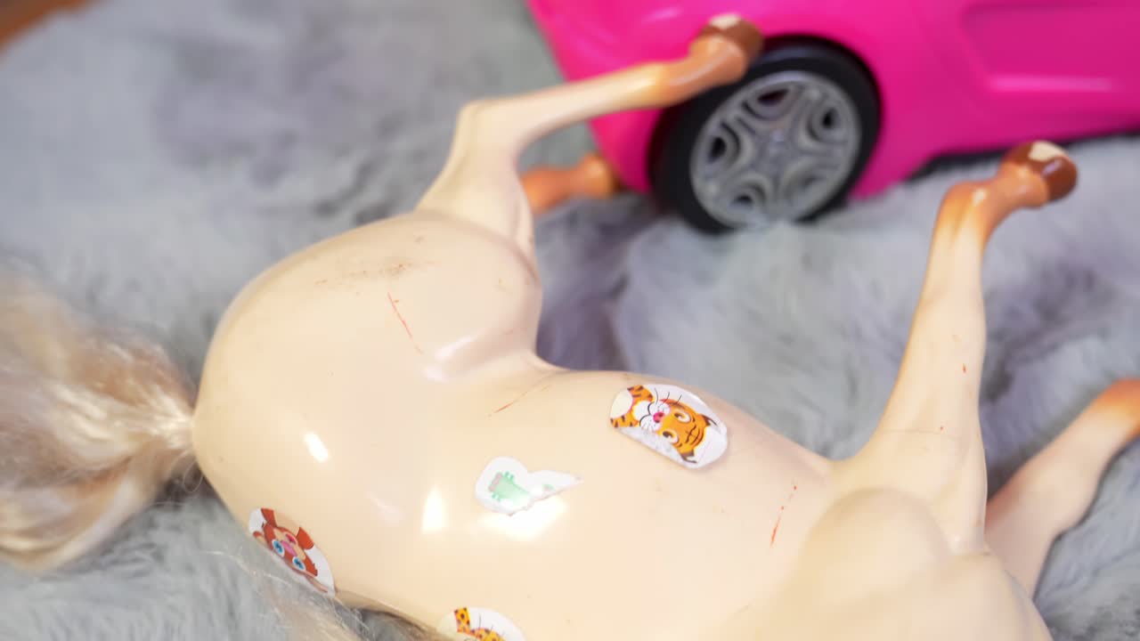 Bir çocuğun oyun odasında yaşanan dağınık bir anı yakalayan, pembe mini bir arabanın yanında kabarık bir halı üzerinde baş aşağı duran, sevimli hayvan çıkartmalarıyla kaplı plastik bir oyuncak atın yakın çekimi