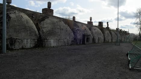 the exterior of the concrete bomb shelter to hide civil people, an underground apocalypse bunker built in old coastal fortification, cloudy spring day with sun, wide handheld shot tilt down