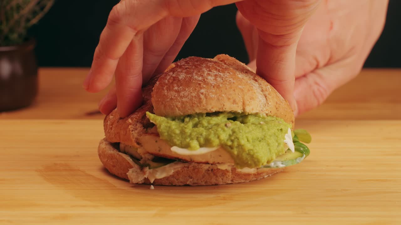 American burger with fish or chiken cutlet, with green salad,onion and guacamole on top close-up. Chef makes burgers without meet. Fast and street food concept. High quality 4k footage