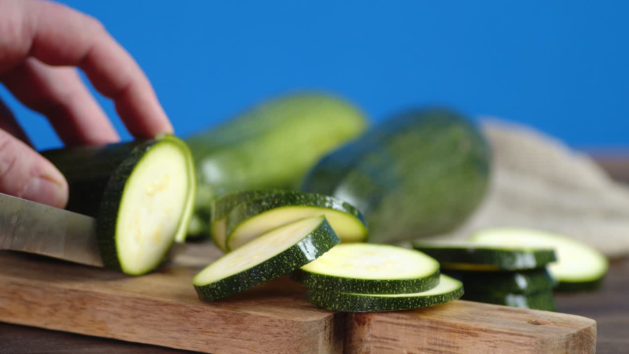 남성의 손이 zucchini를 작은 조각으로 잘라내고 있습니다.
