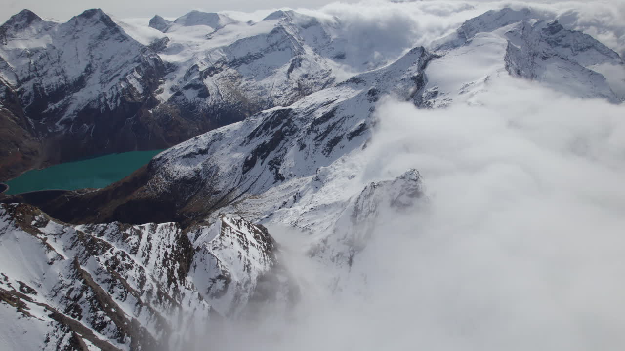 vuelo aéreo de pájaros sobre las montañas nevadas de austria durante el día nublado y soleado - hermoso lago en el valle