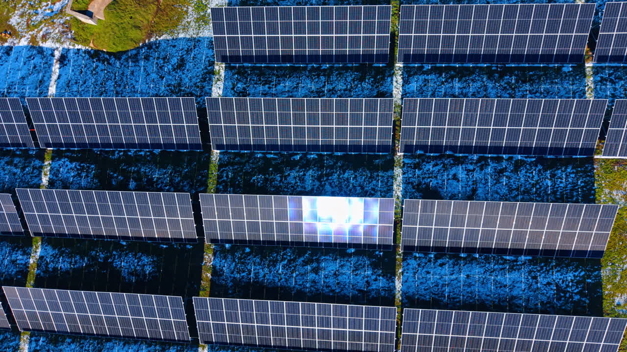 Infrastruttura di impianto solare con piccolo edificio in cemento. Vista aerea di pannelli fotovoltaici su terreno innevato accanto a una piccola struttura di servizio o cabina di trasformazione