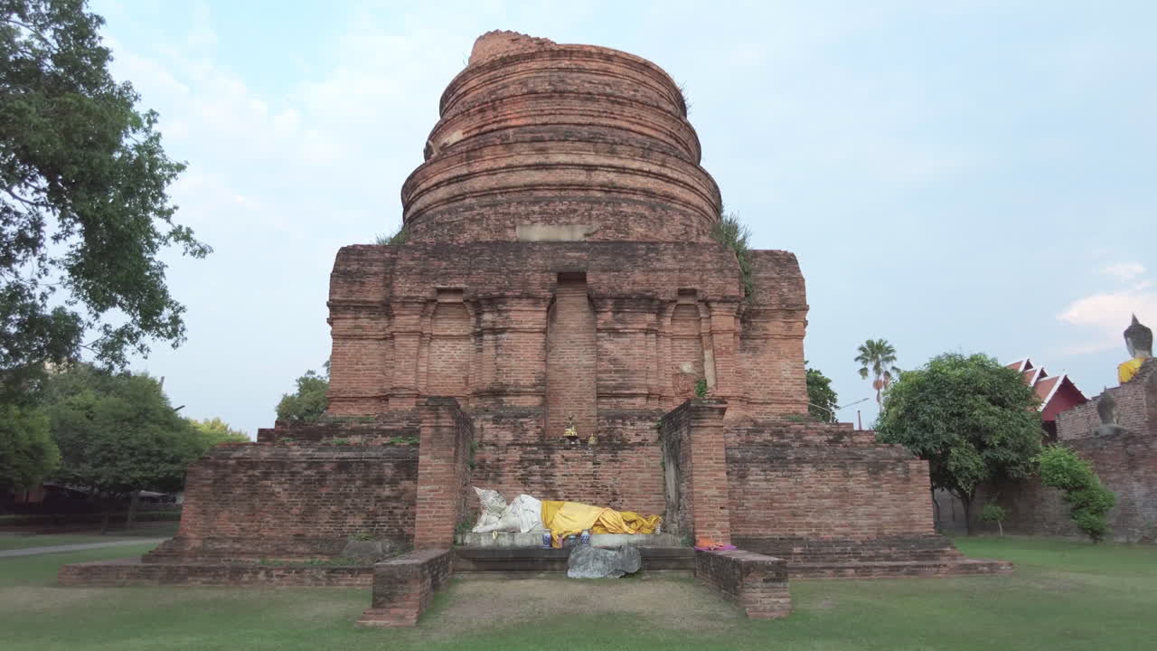 Ancient brick stupa under clear sky with draped yellow cloth and Buddha statue remnants at a serene temple in Ayutthaya,Thailand