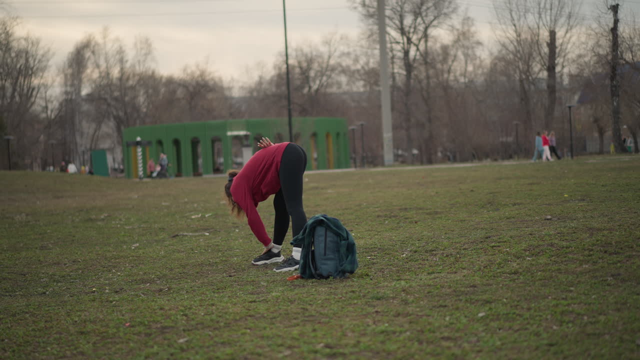 White Woman Tying Running Shoes In Park Bending To Lace Sneakers Beside Backpack On Grass, PreRun Ritual, Measured Breathing And Focused Posture Before Jog Through Urban Green Space