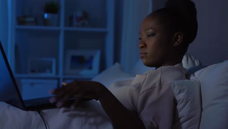 African-Woman-Using-Laptop-in-Bed-at-Home-at-Night.technology,-internet,-communication-and-people-concept-tired-young-african-american-woman-opening-laptop-computer-in-bed-at-home-at-night