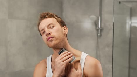 a handsome man in a t-shirt shaves with a shaver in the bathroom